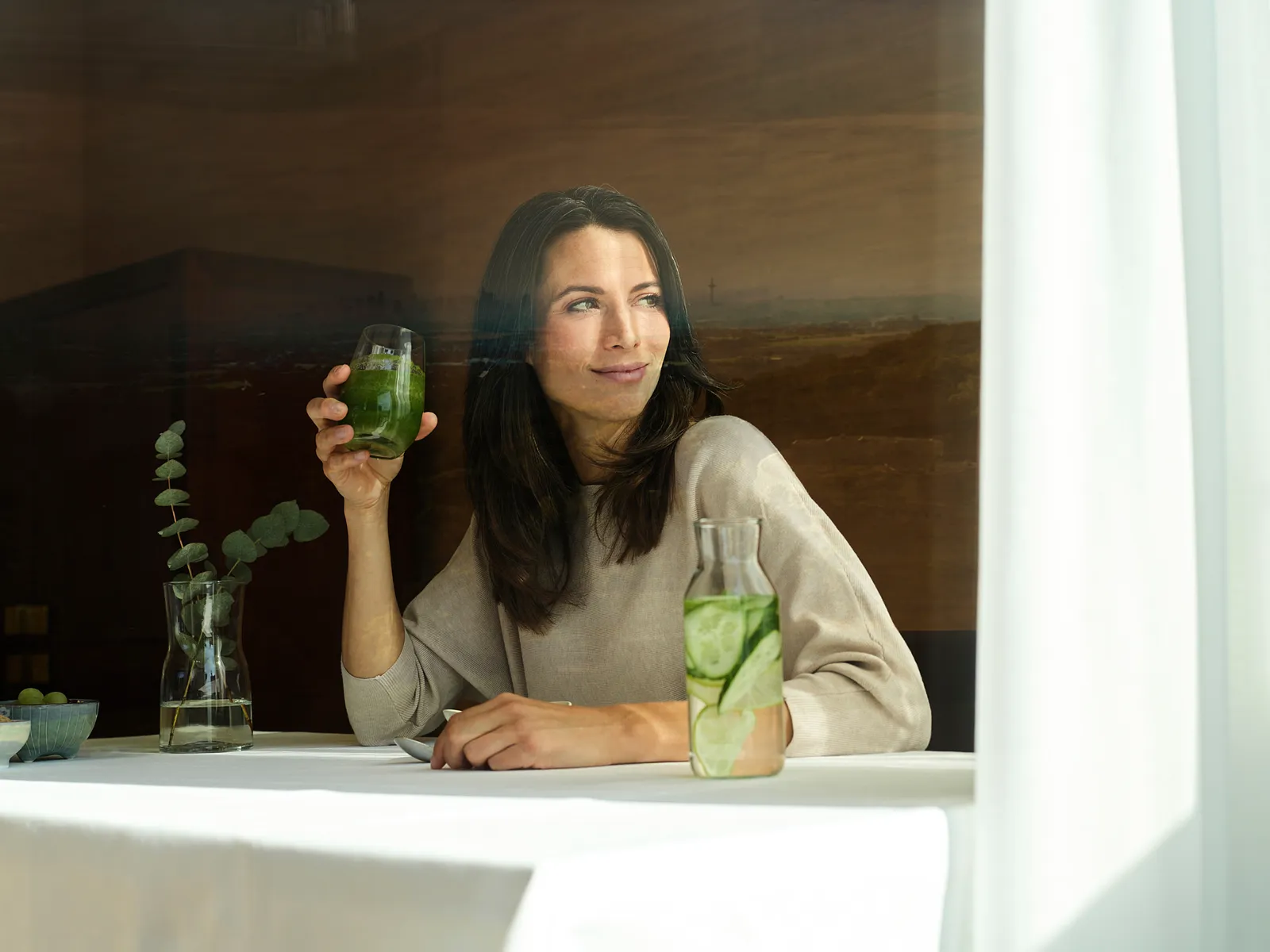 Frau mit grünem Smoothie am Fenster mit Blick über den Taunus