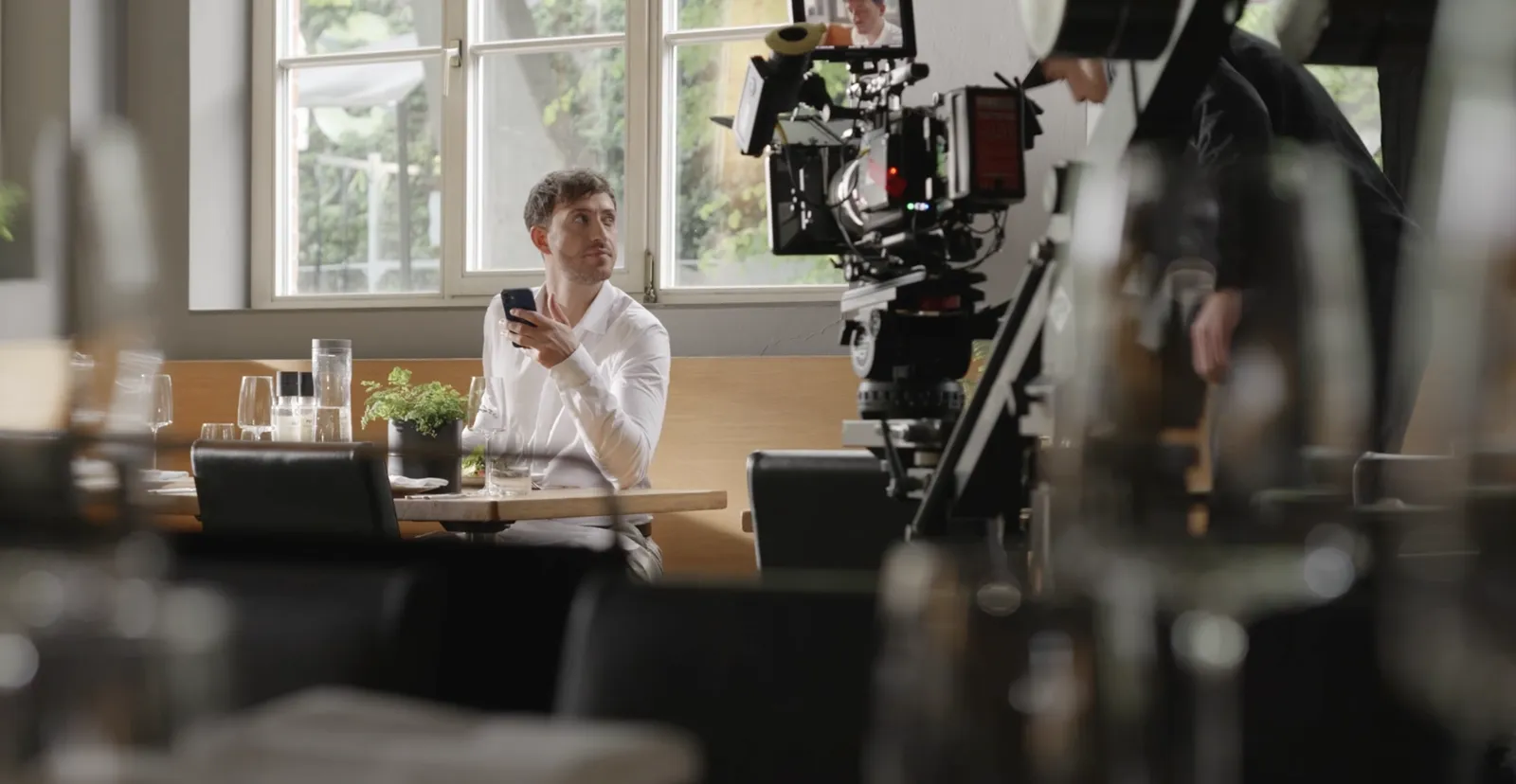 Dreh in einem Restaurant, ein Darsteller mit Smartphone sitzt am Tisch vor der Filmkamera