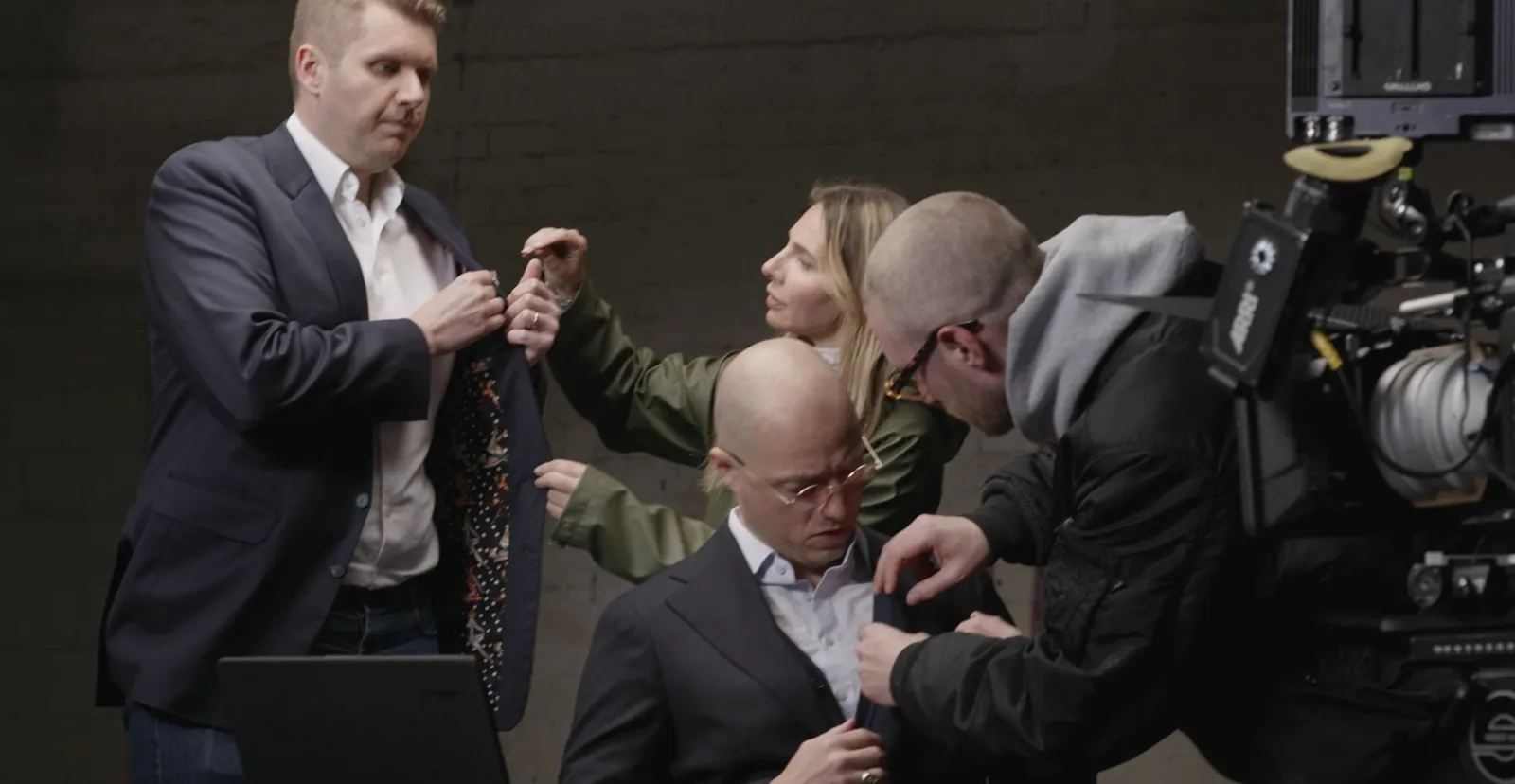 Styling am Set, die Crew richtet Jackett und Hemd zweier Darsteller neben der Filmkamera