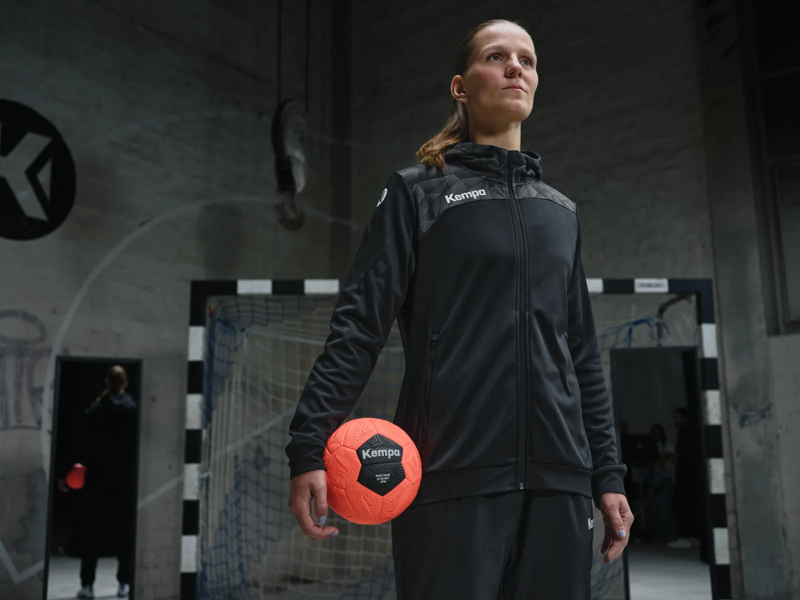 Spielerin in Kapuzenjacke mit orangem Ball vor dem Tor