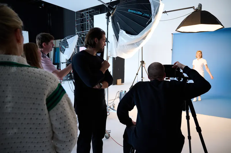 Das Team verfolgt das Shooting vor hellblauem Hintergrund unter großen Lichtschirmen