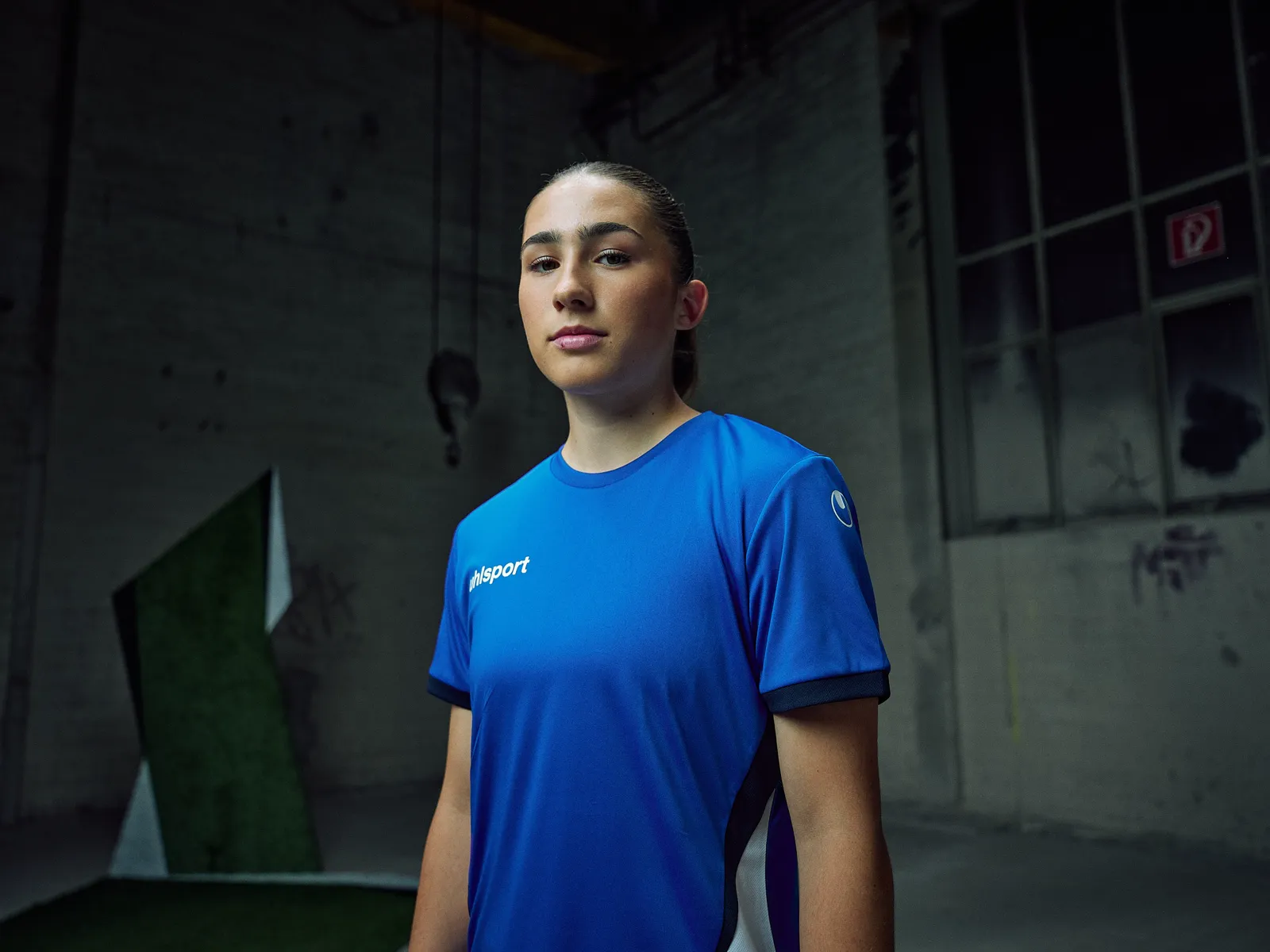 Spielerin im blauen Trikot, Porträt in der dunklen Halle
