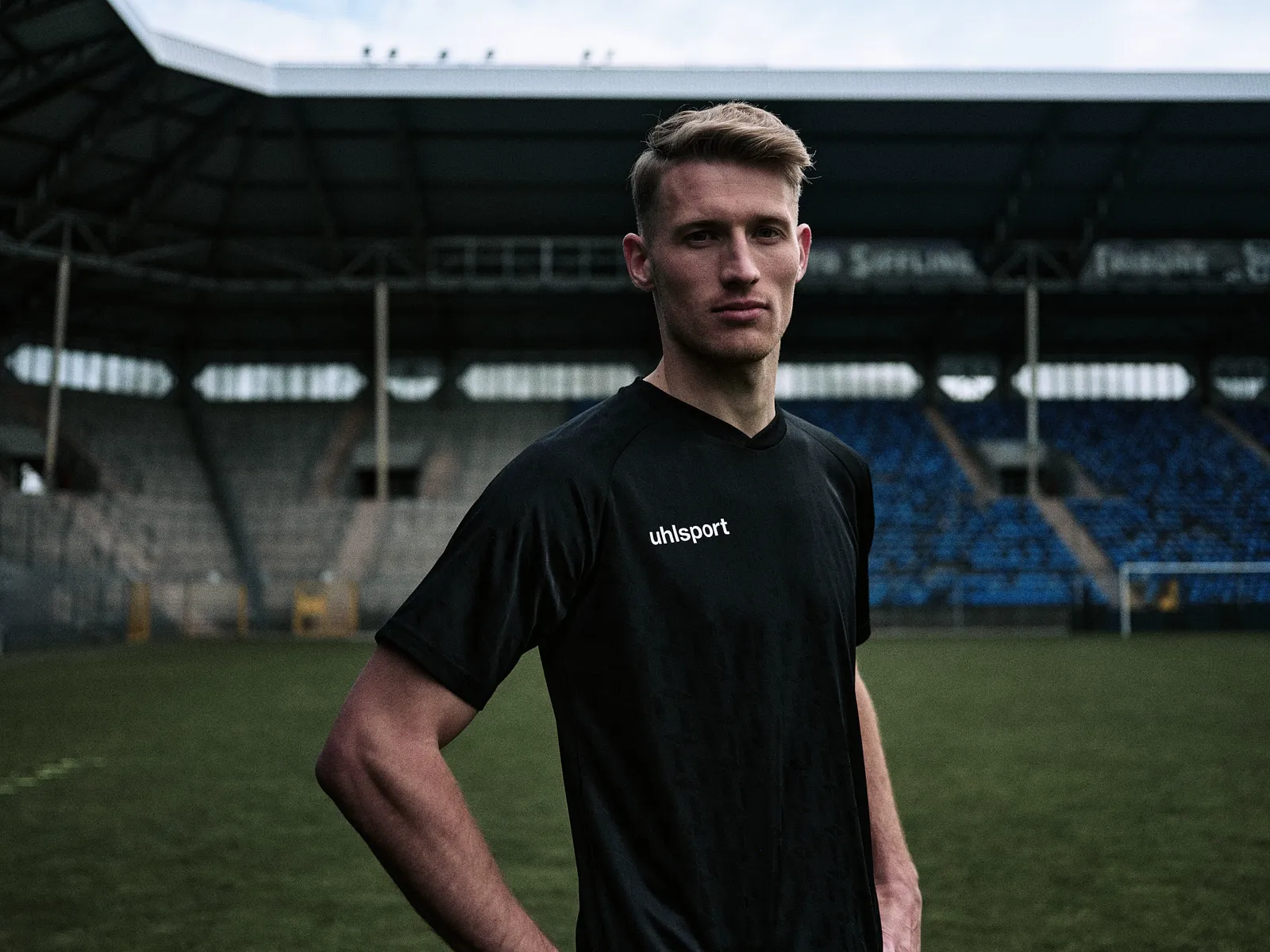 Spieler im weißen Shirt mit Händen an den Hüften vor der Tribüne